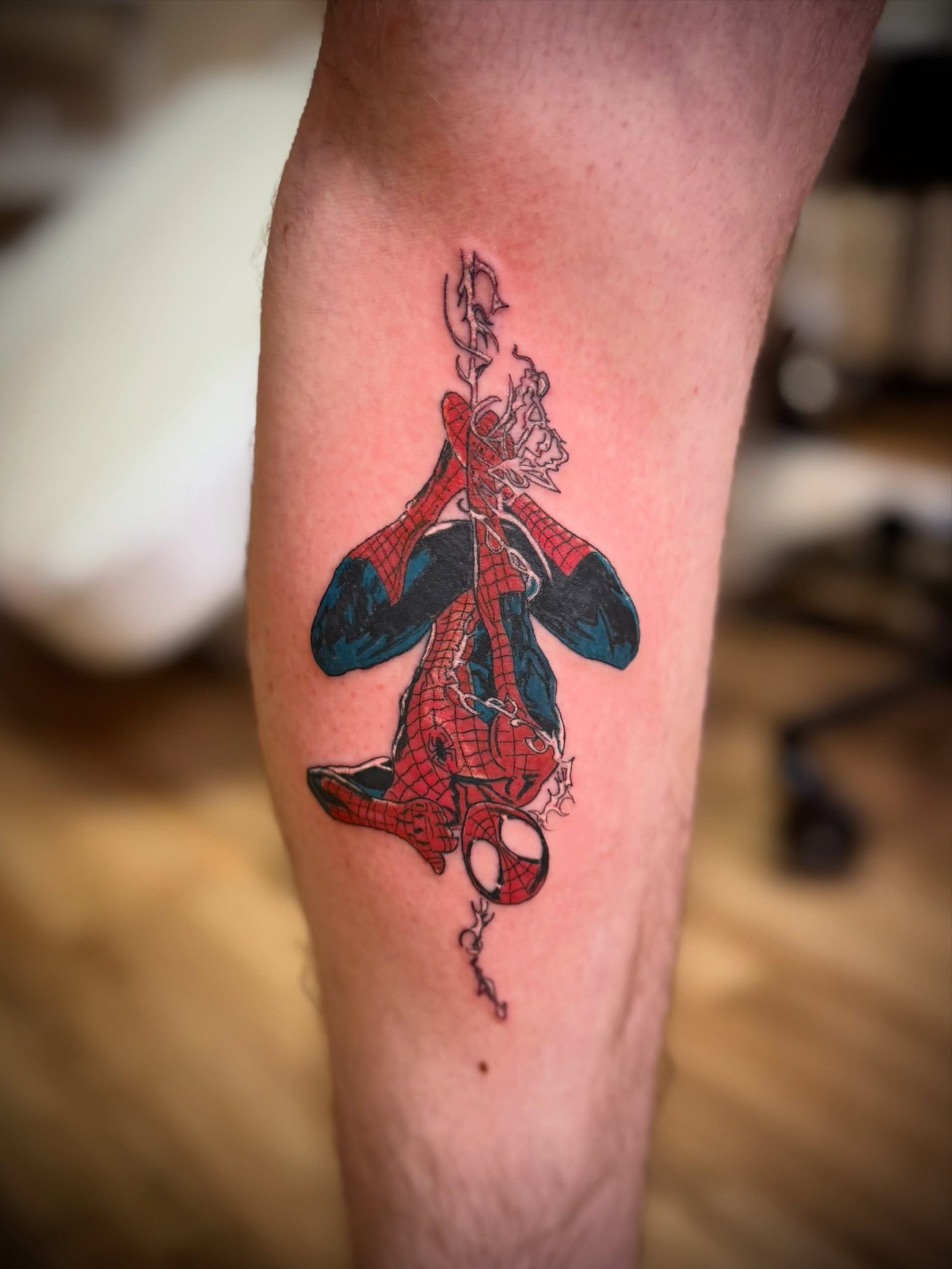 Spider-Man hanging upside down, tattooed in full colour on a calf